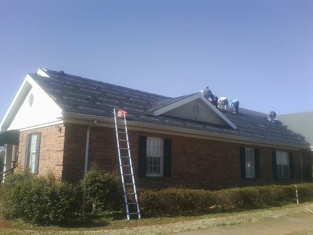 Crew tearing shingles off a brick ranch roof with a ladder set — Emergency Roof Repair work by our crew in Putnamville