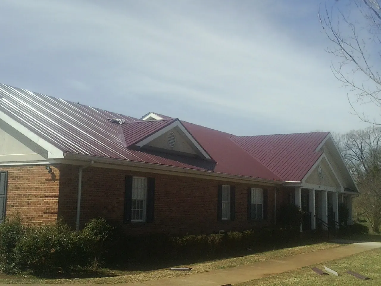 Red metal roof with gabled entries on a long brick building, from a Hail Damage Roof Repair job in Putnamville
