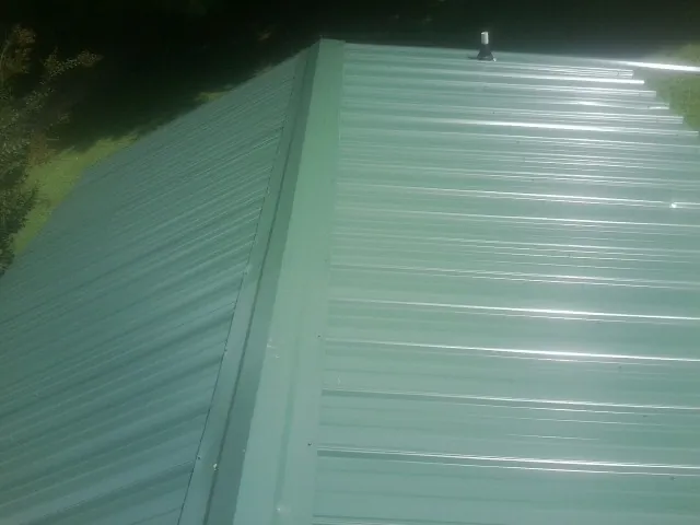 New green metal panels meeting at the ridge of a roof — Flat Roof Repair work by our crew in Putnamville