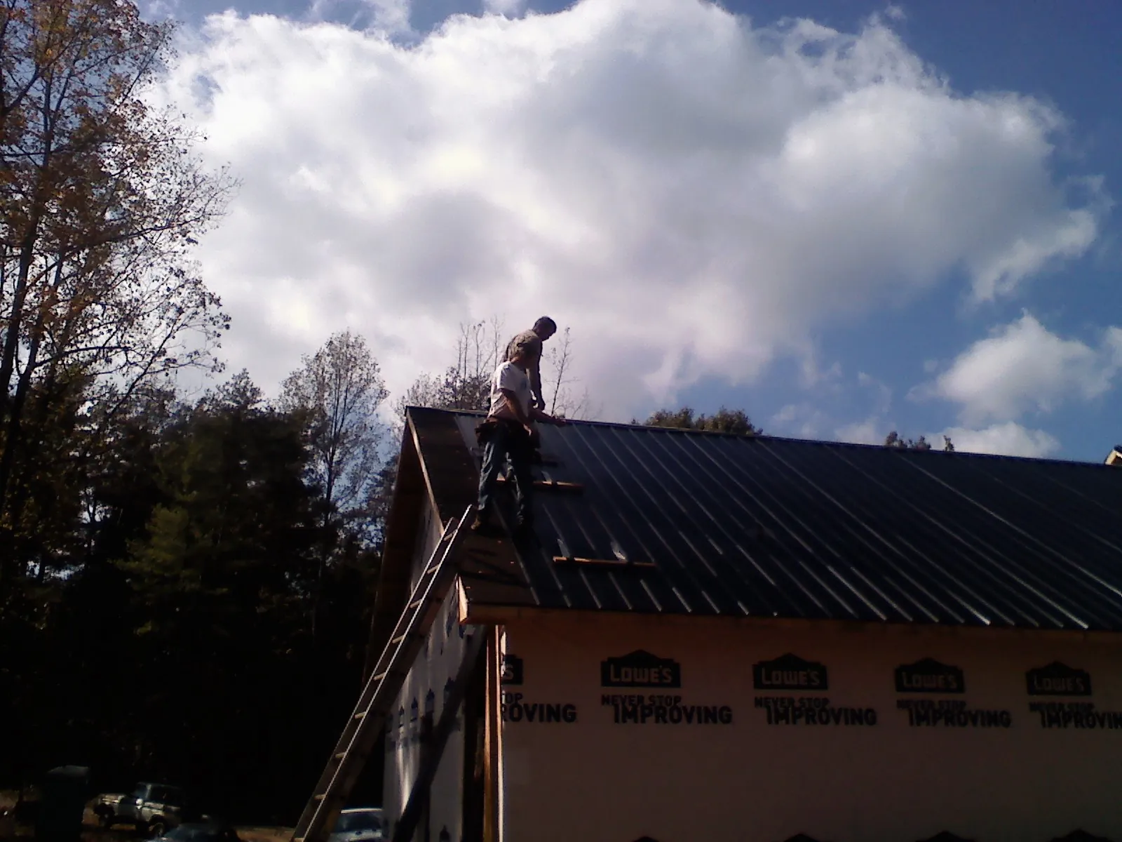 Roofer fastening dark metal panels high against a cloudy sky, from a Roof Inspection job in Putnamville