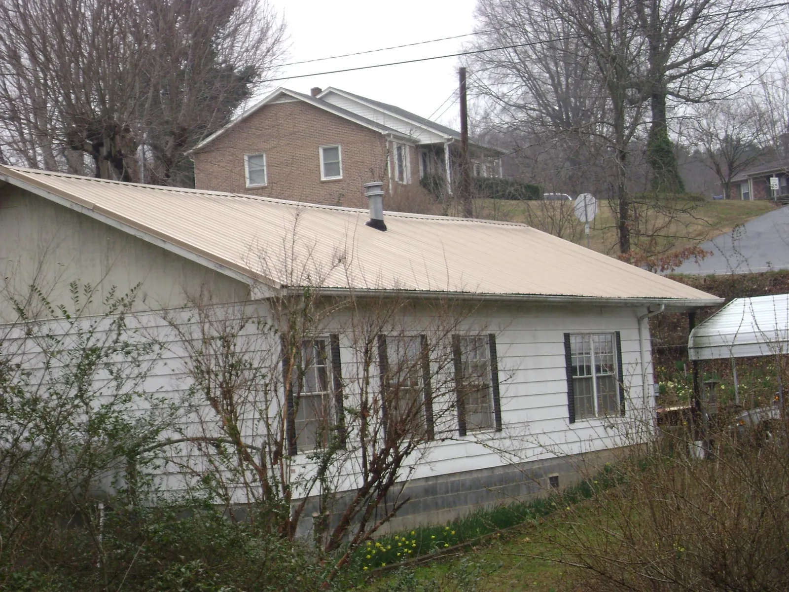 Tan metal roof on a white sided house set into a hillside — Commercial Roofing by Roofing Brothers in Putnamville
