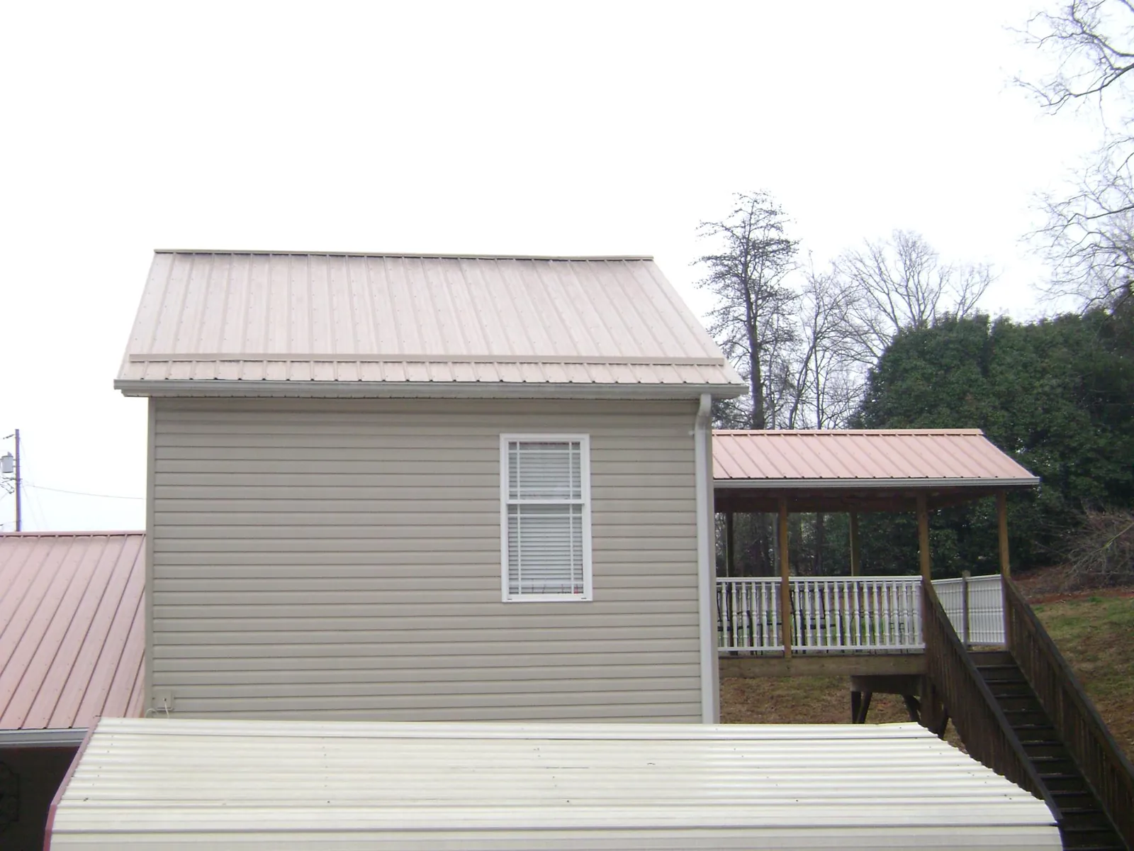 Tan metal roofs on a two story addition and attached porch, from a Roof Replacement job in Putnamville
